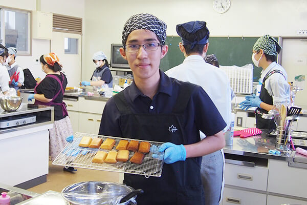 焼き上がったフィナンシェを持つ家庭科部部長のK.S.さん